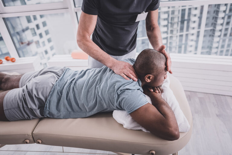 Underdo this problem. Competent therapist touching forehead of his patient while going to do massage